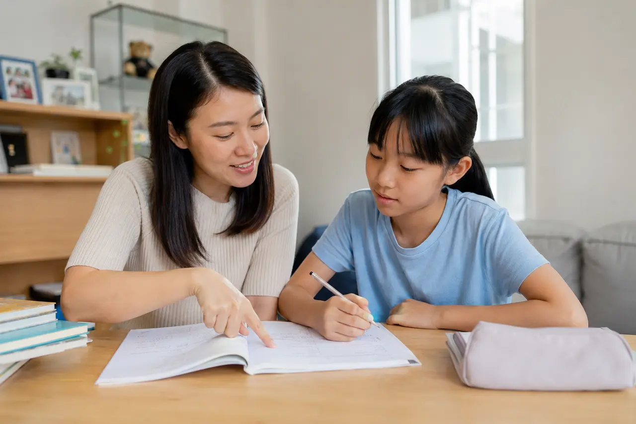 Chinese female tutor guiding a school-aged child through an open workbook